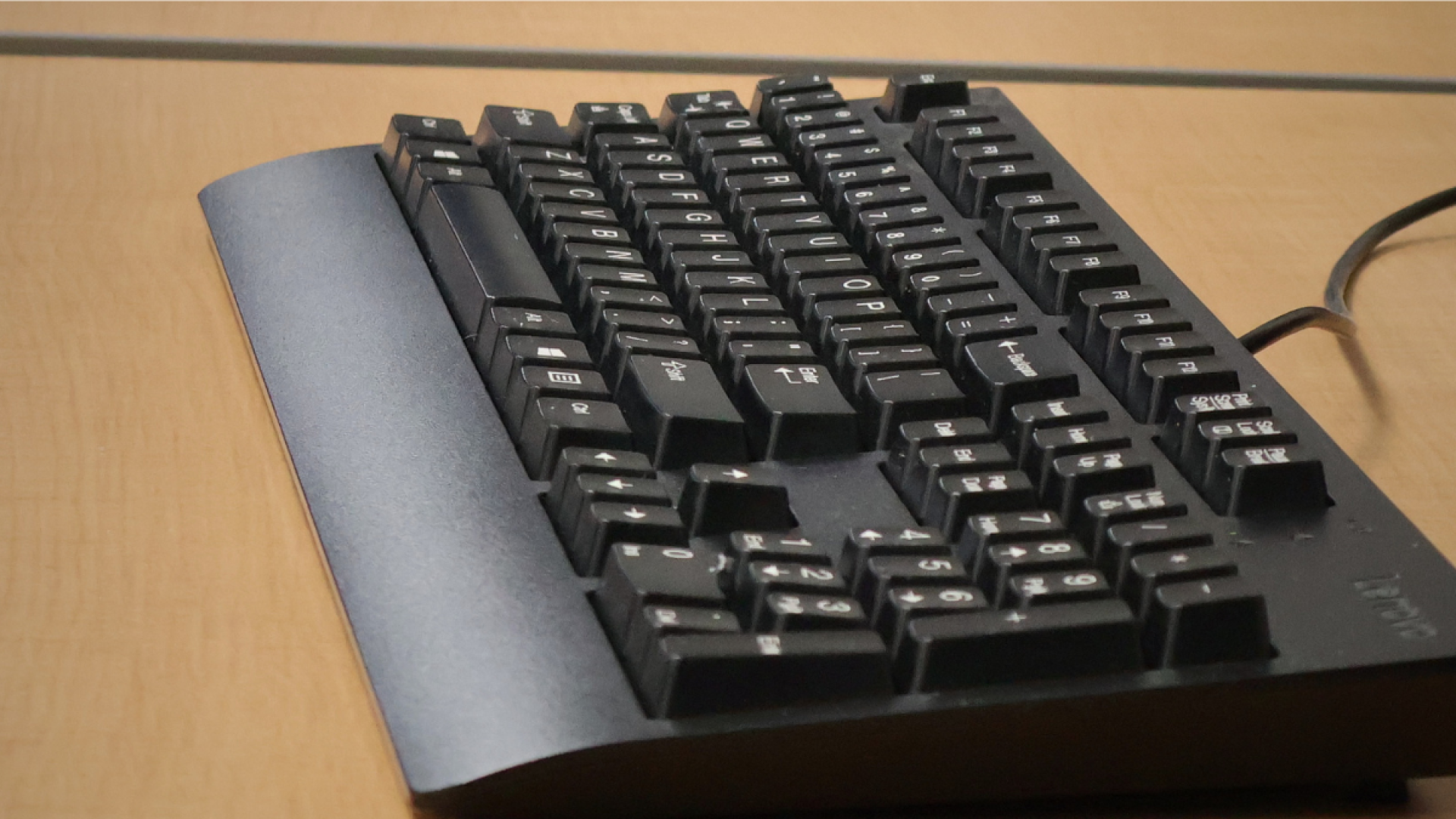 Close-up of a black computer keyboard on a wood desk in a BRTC computer lab.